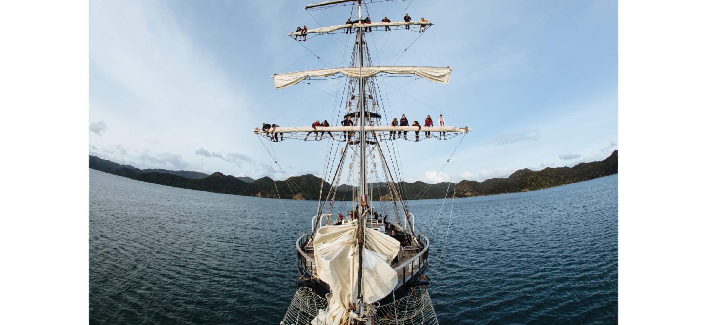 A view of the back of the Spirit of Adventure with passengers climbing across two of the yacht’s masts.